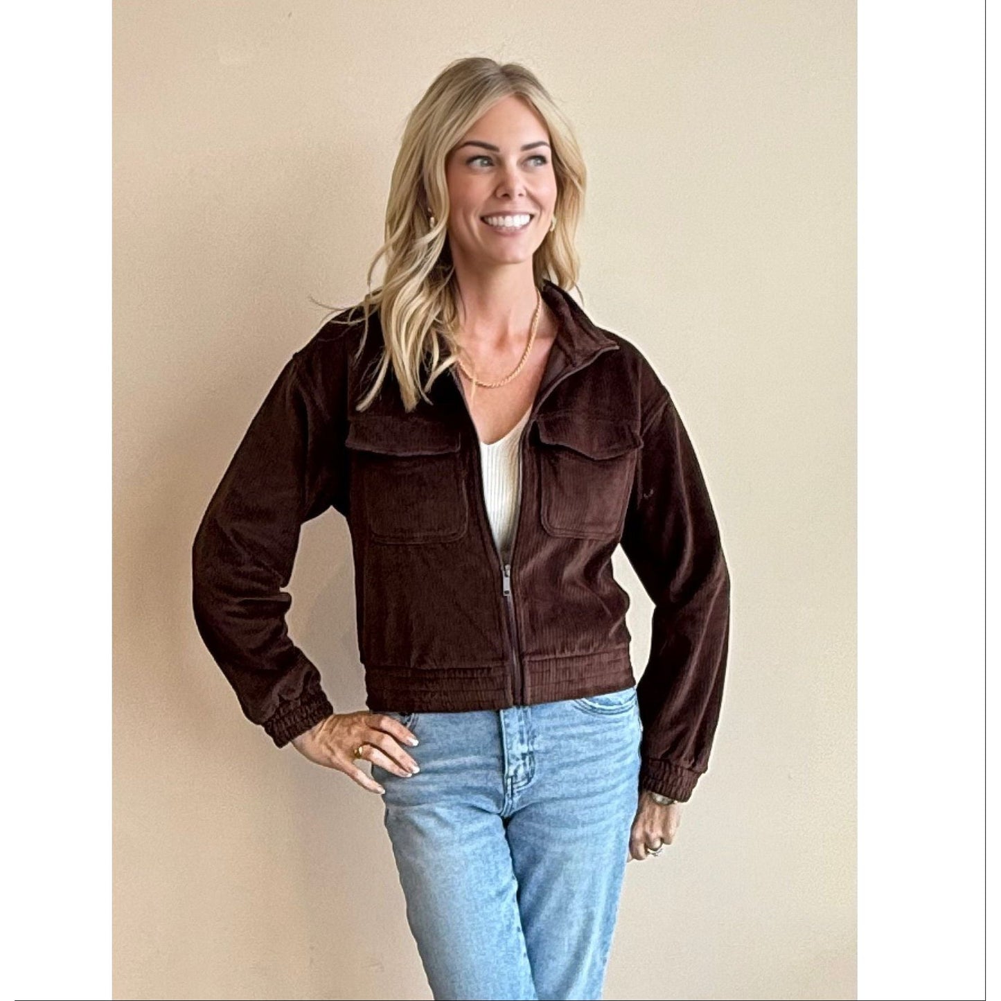 Woman wearing a brown jacket and blue jeans against a beige background