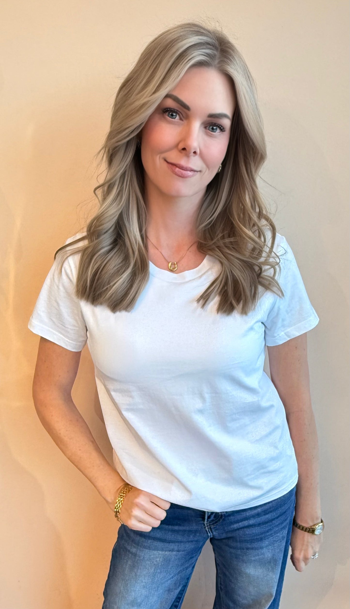Woman wearing a white t-shirt and blue jeans against a beige background