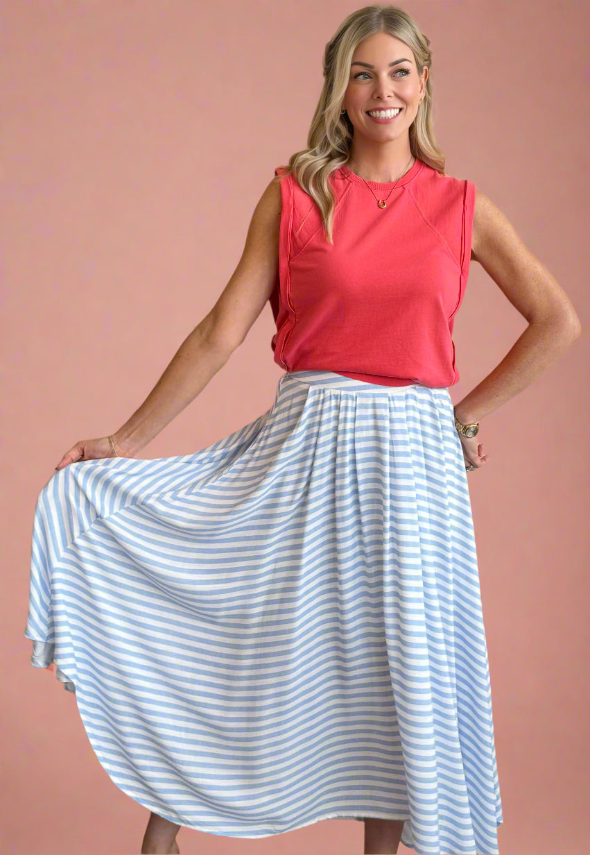 Woman wearing a red sleeveless top and blue and white striped skirt against a beige wall.