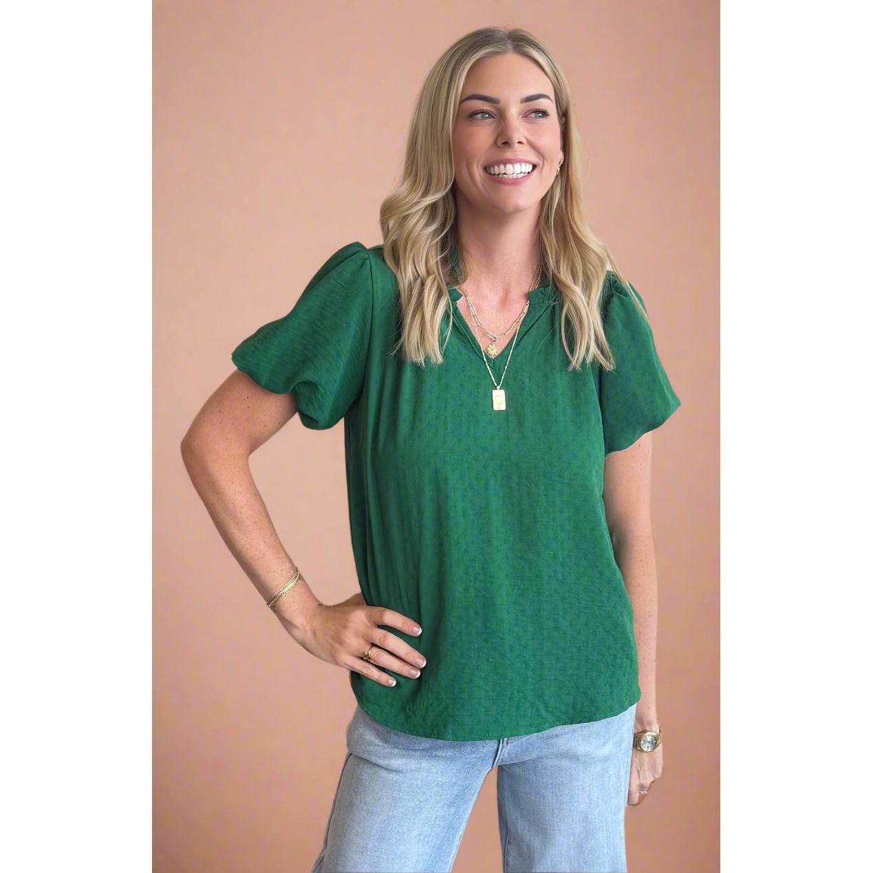 Woman wearing a green blouse and light blue jeans against a beige background