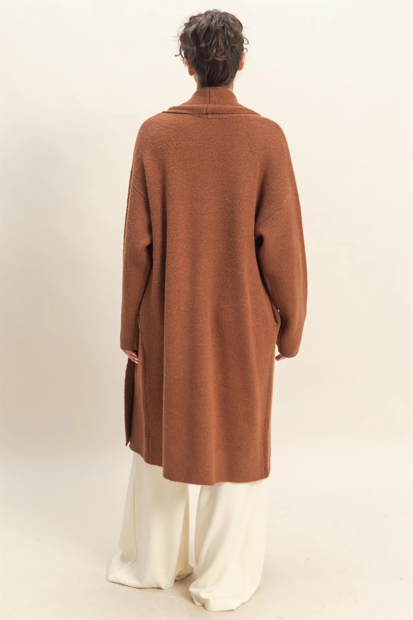 Person wearing a brown coat and white pants on a plain background