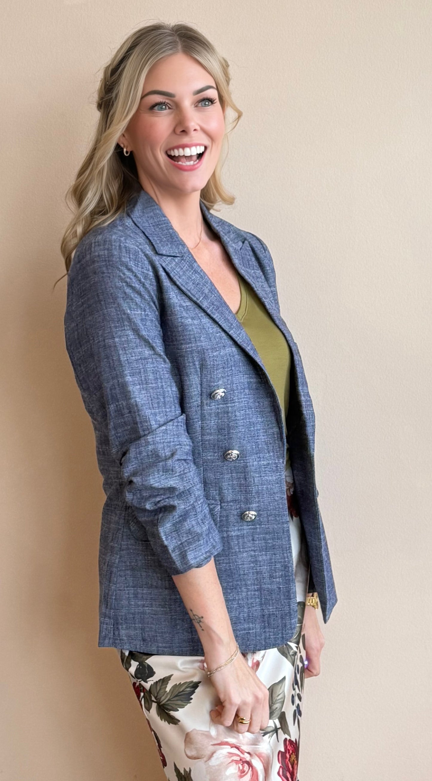 Woman wearing a blue blazer over a green top with floral pants against a beige background