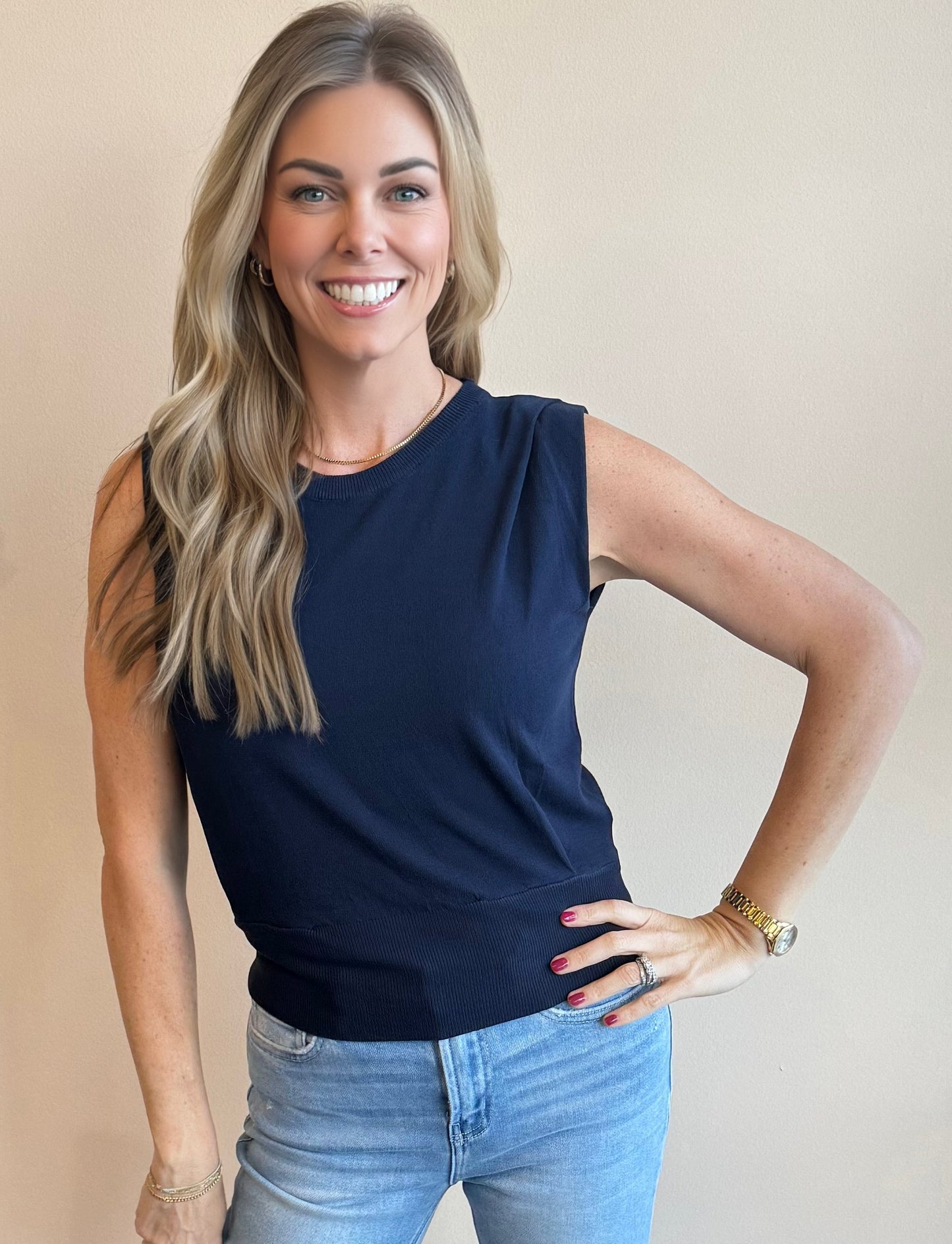 Woman wearing a navy sleeveless vest top and light blue jeans against a beige background