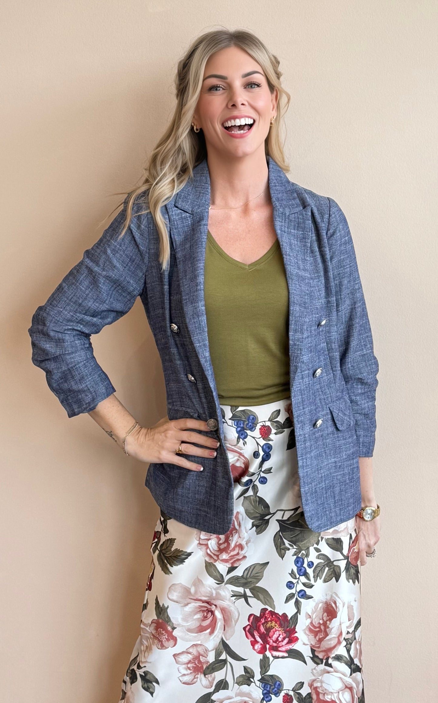 Woman wearing a blue cardigan, green top, and floral skirt against a beige background