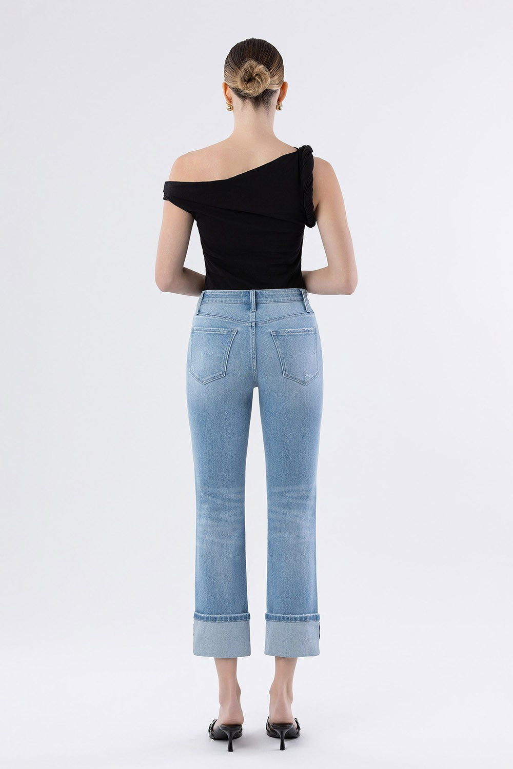 back side of person wearing a black off-shoulder top and light blue jeans on a white background