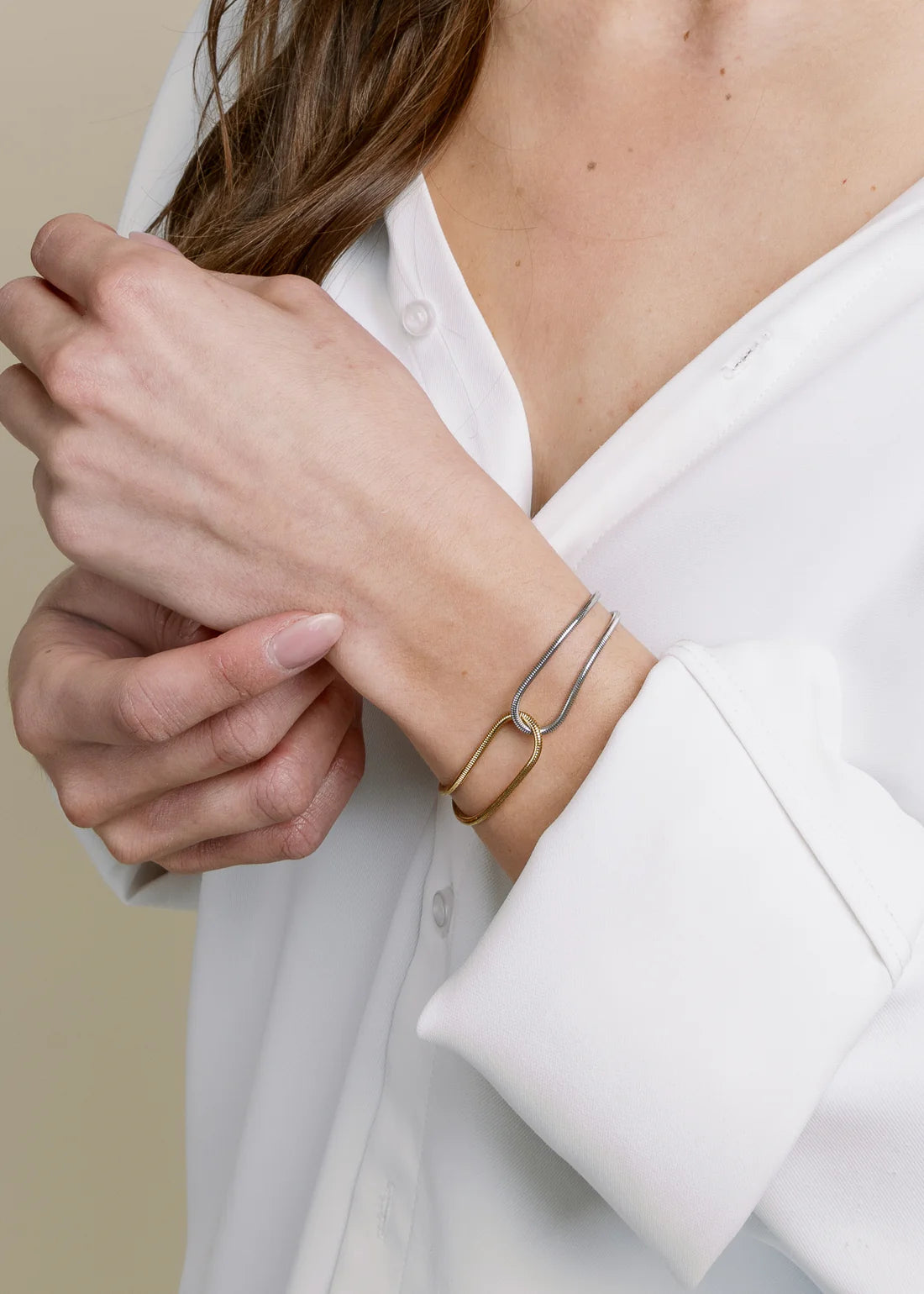 Person wearing a white shirt with a mixed-metal bracelet on a neutral background