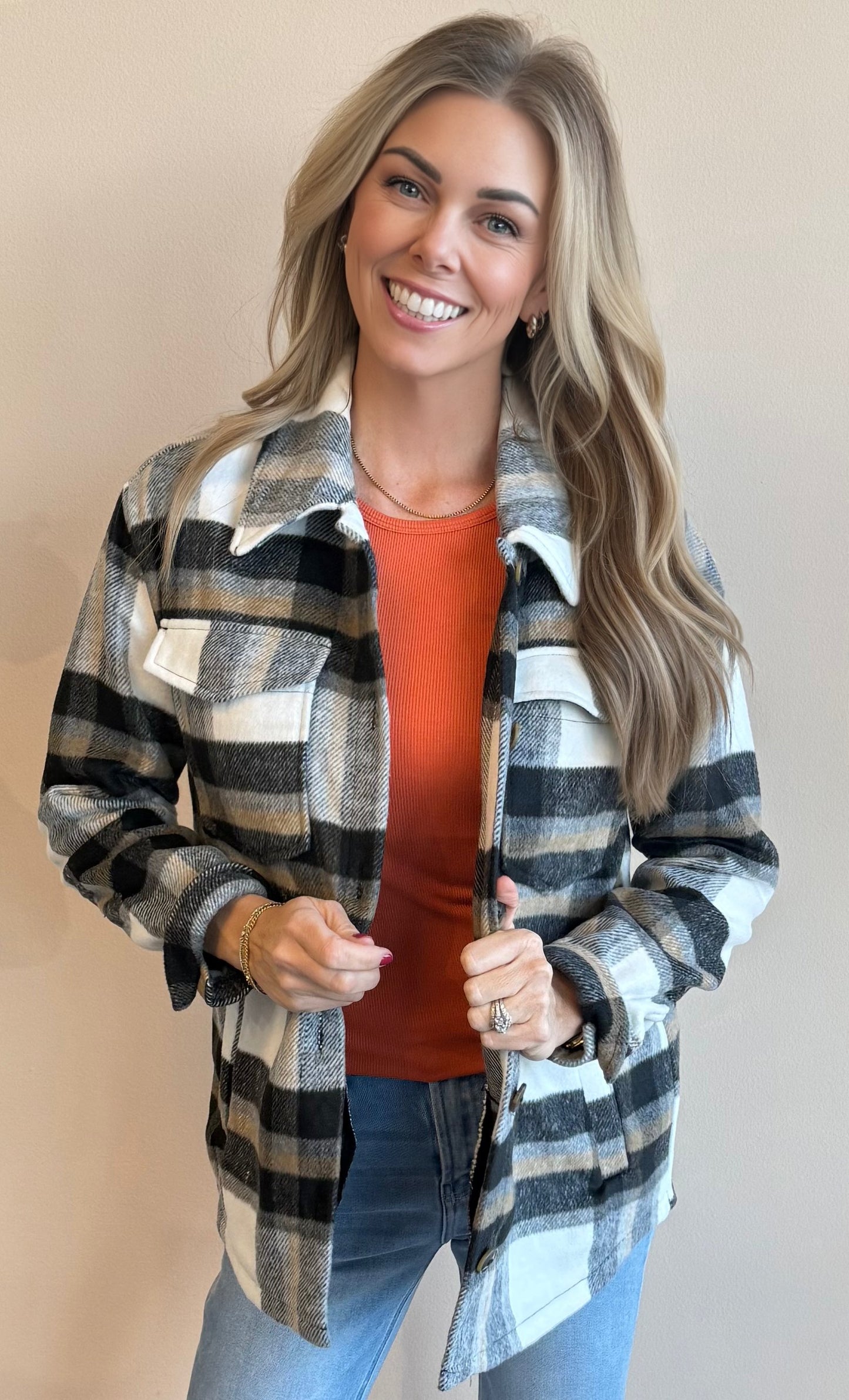 Woman wearing an unbuttoned black plaid shacket over an orange top with a beige background