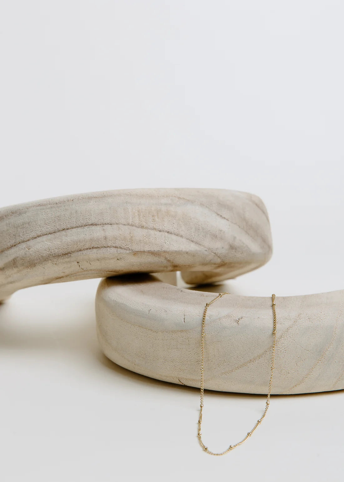 Two beige ceramic rings stacked on a light gray background with a simple gold necklace draped over it