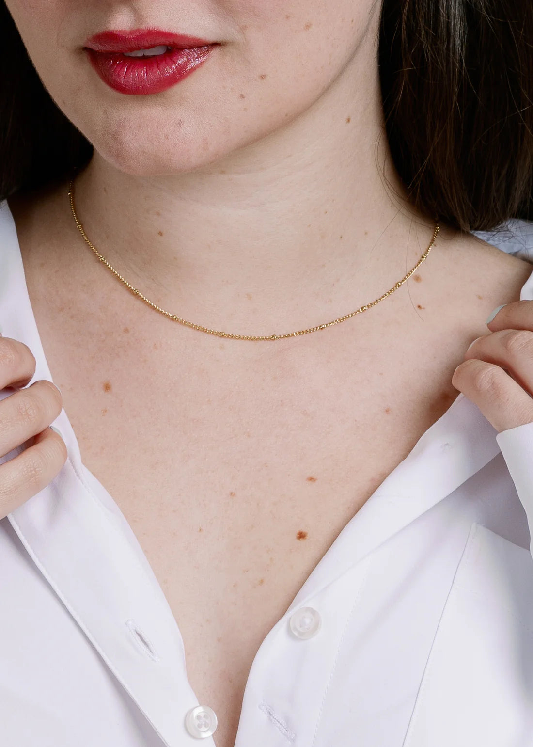 Close-up of a person wearing a gold necklace with a white shirt.