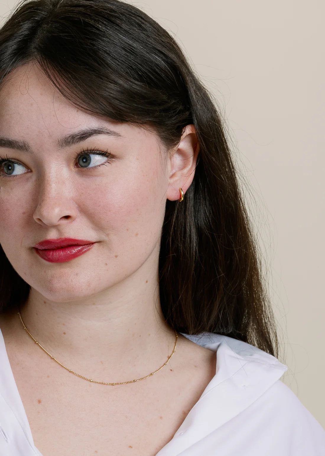 Close-up of a woman wearing a gold necklace and earring against a beige background