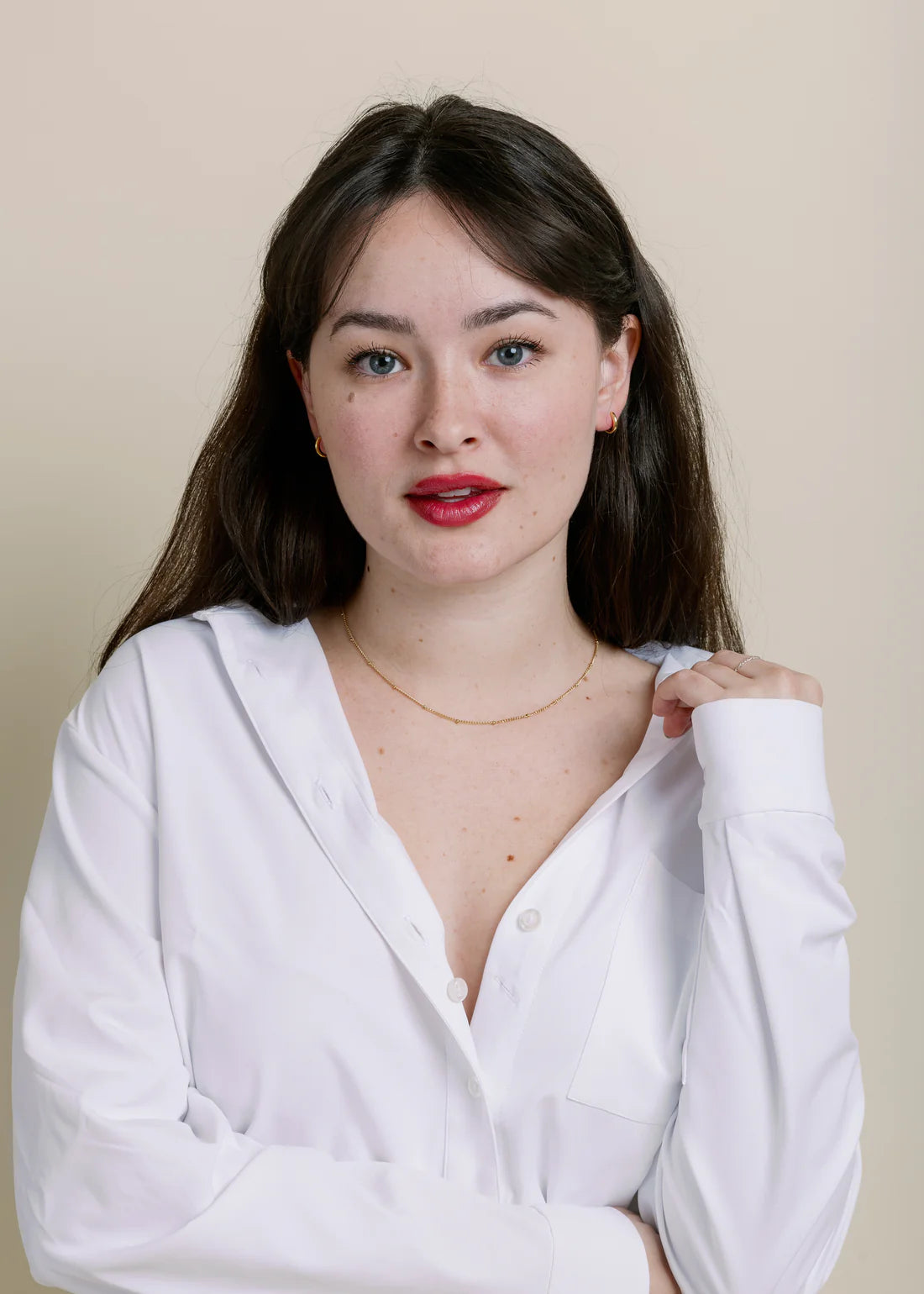 Woman wearing a white shirt with simple gold necklace against a beige background