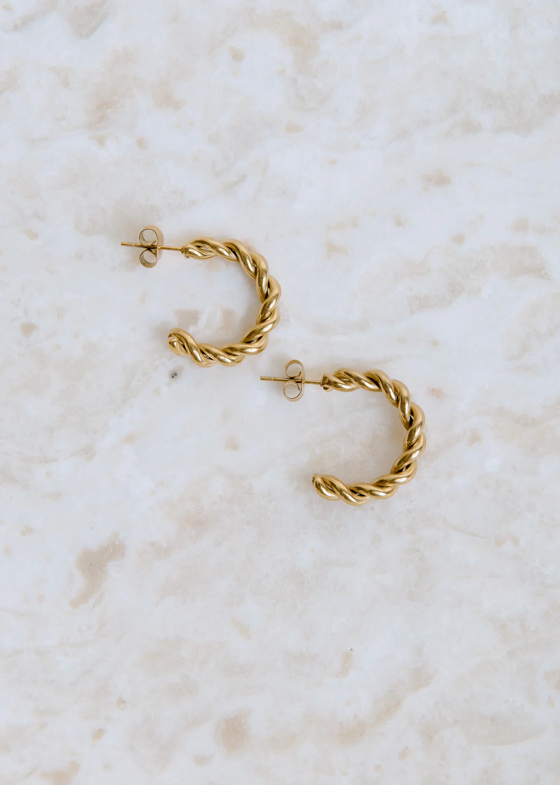 Gold hoop earrings on a light marble background