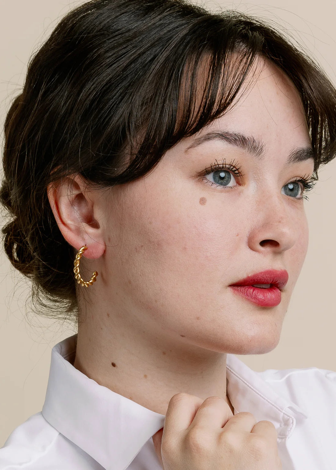 Woman wearing gold hoop earrings against a beige background