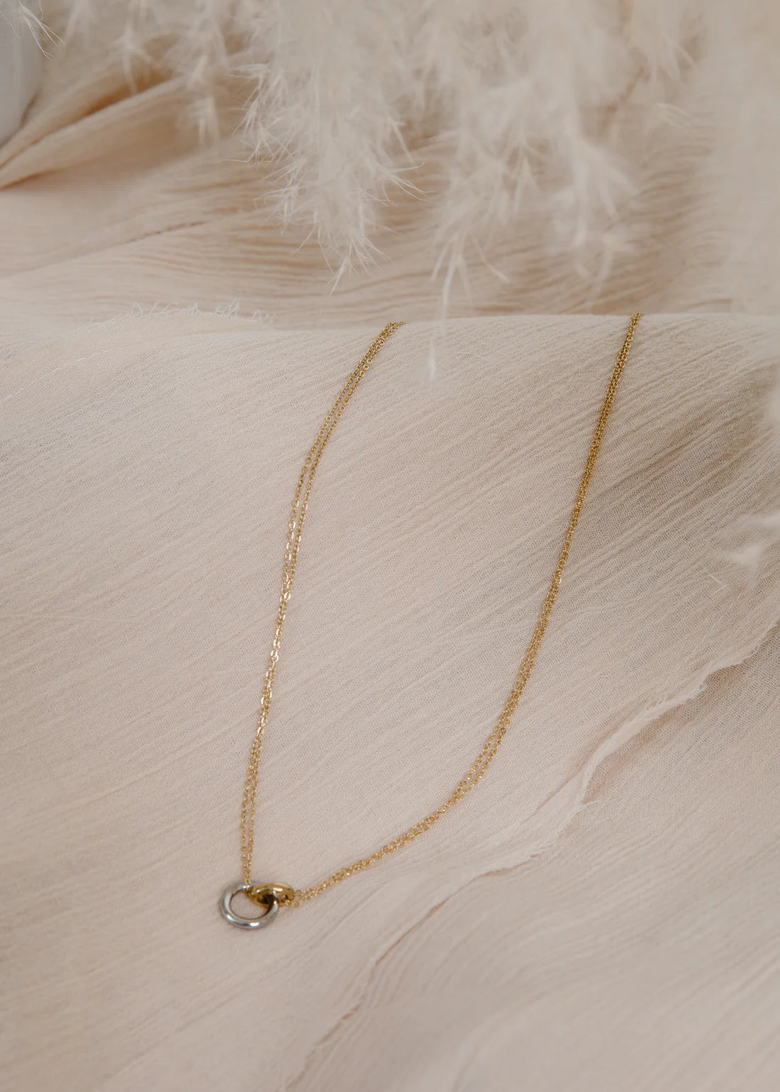 mixed-metal small circles necklace on a soft beige fabric background