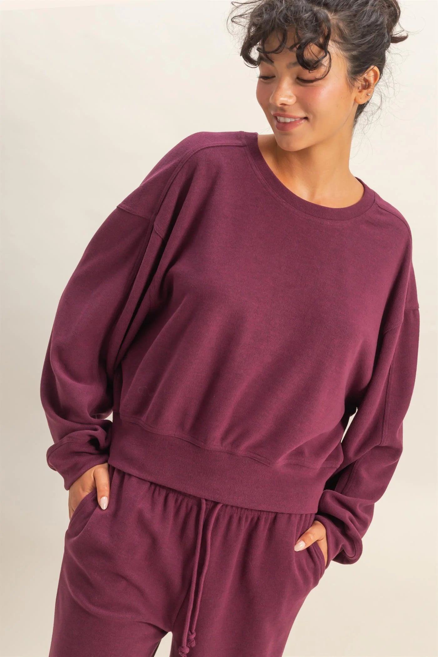 Woman wearing a maroon sweatshirt and pants on a beige background