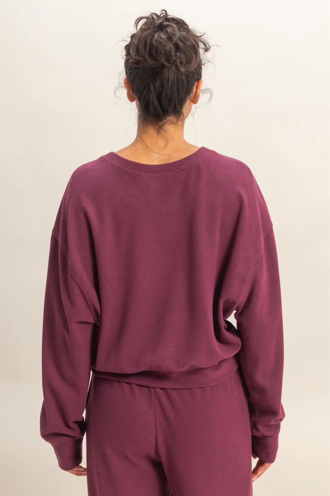 Person wearing a maroon, dark cherry, wine colored sweatshirt and pants on a plain background