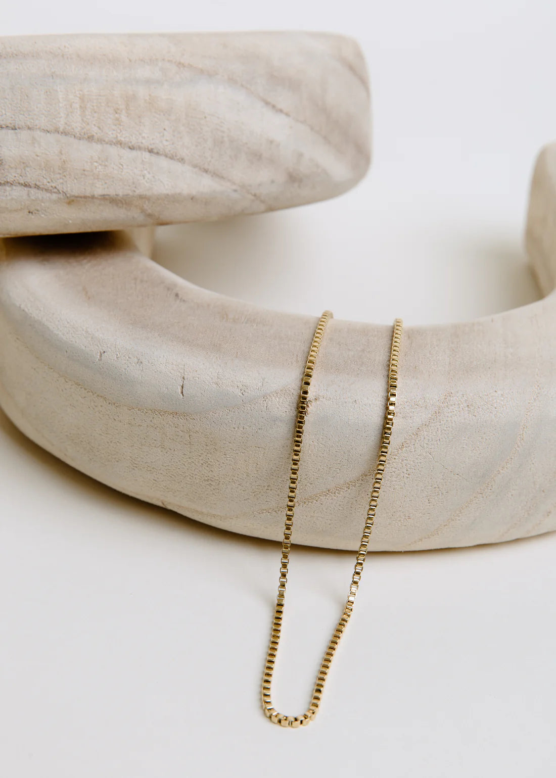 Gold chain necklace on a white surface with a neutral background