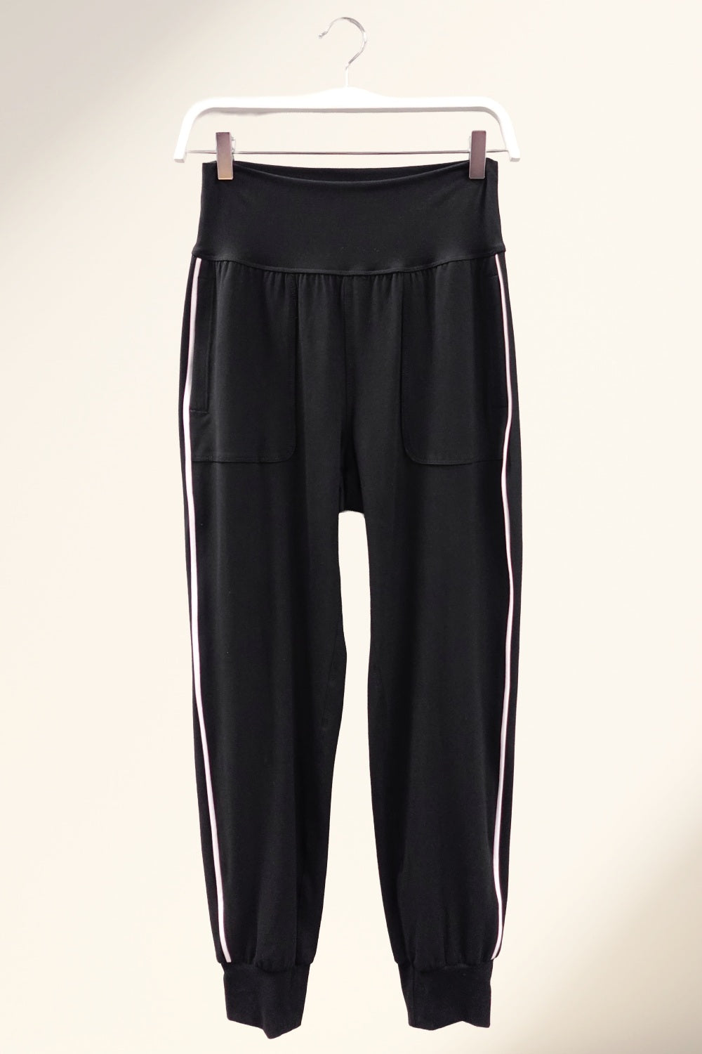 Rae Black jogger pants with white stripes on a hanger against a beige background
