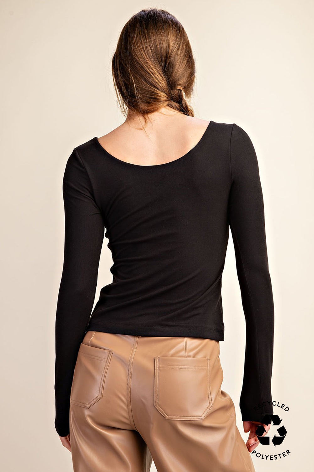 Person wearing a black long-sleeve top and beige pants on a beige background