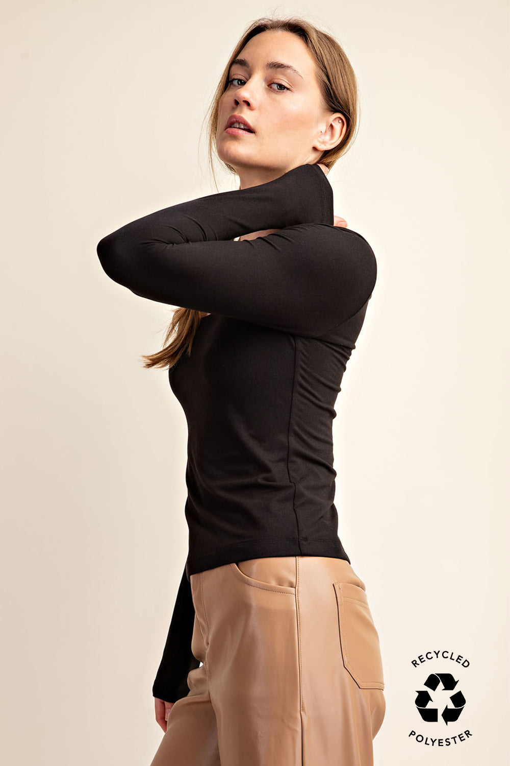 Woman wearing a black long-sleeve top and beige pants on a beige background with a recycled polyester label.