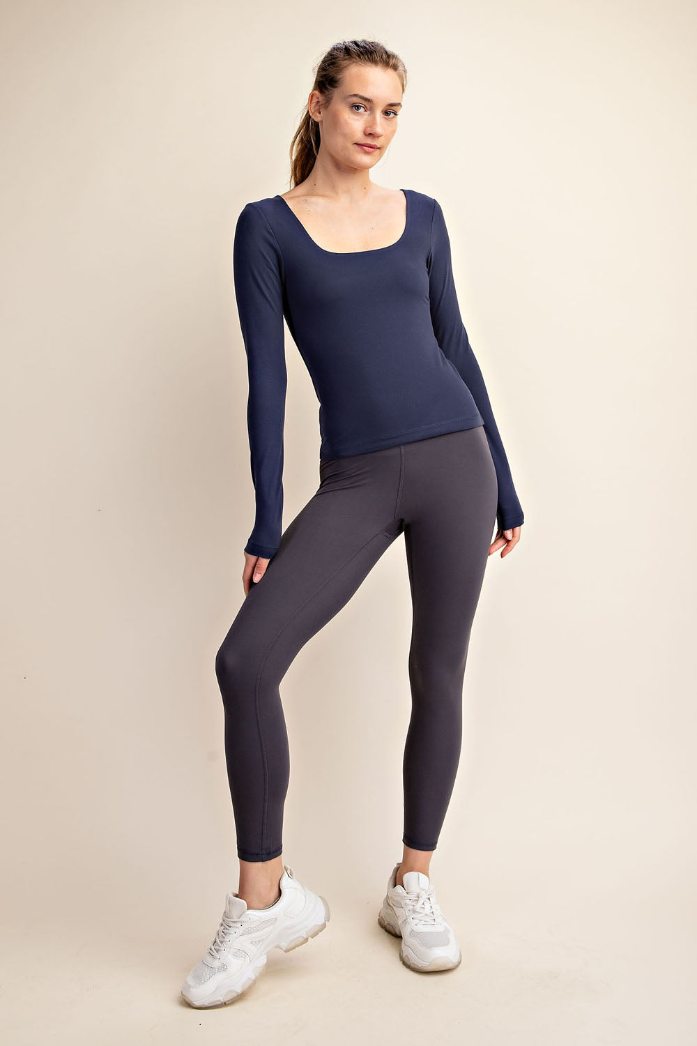 Woman wearing a navy long-sleeve top and dark gray leggings on a beige background