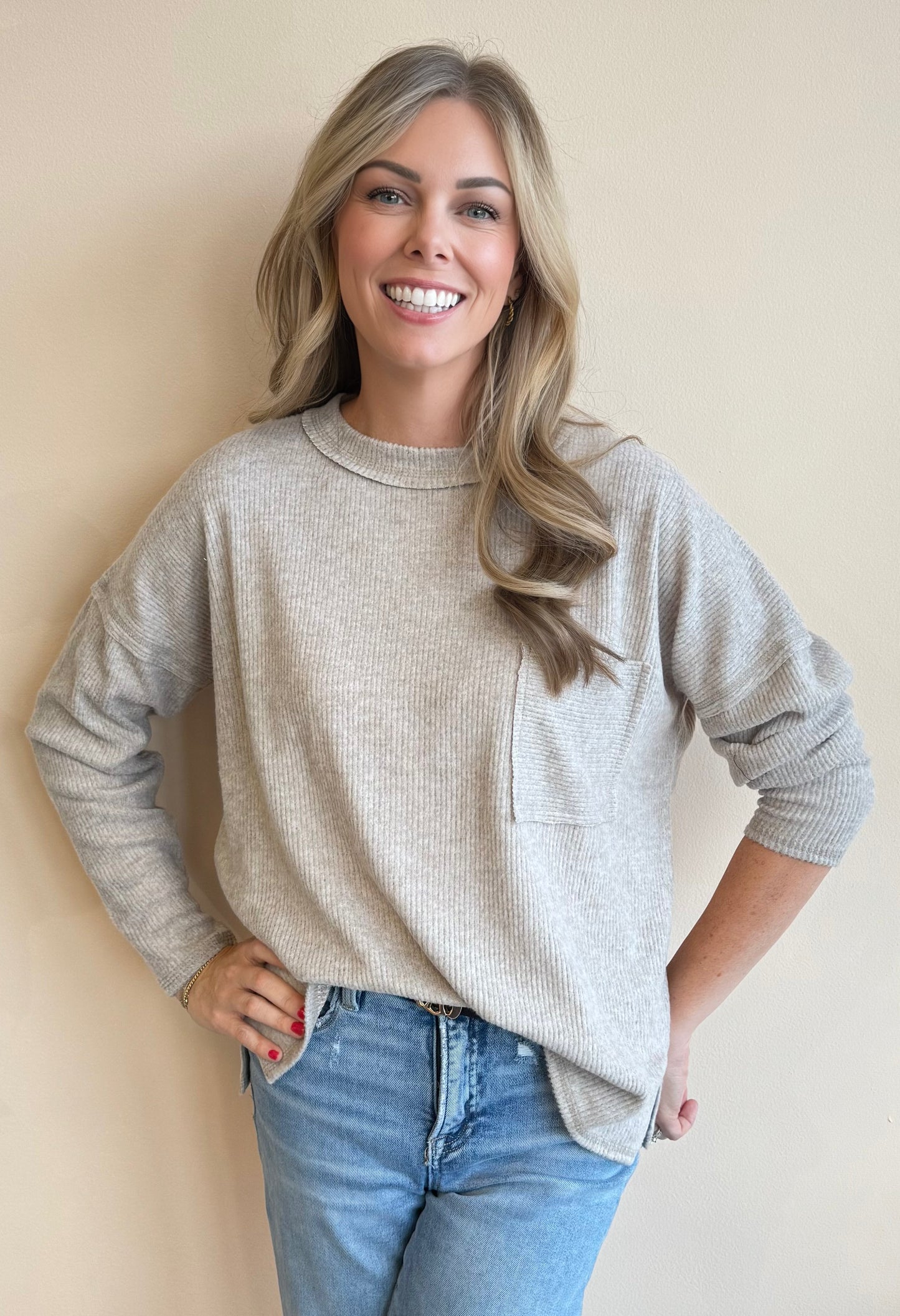 Woman wearing a beige sweater and blue jeans against a beige background