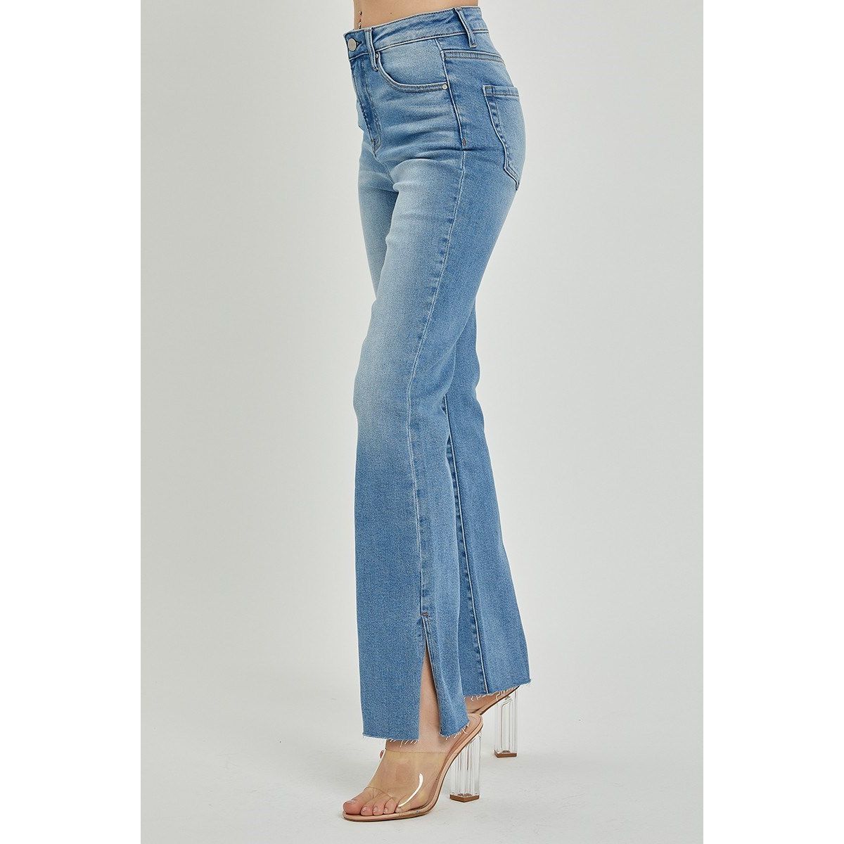 High rise bootcut blue jeans with raw cut hem and side slit detail on a gray background