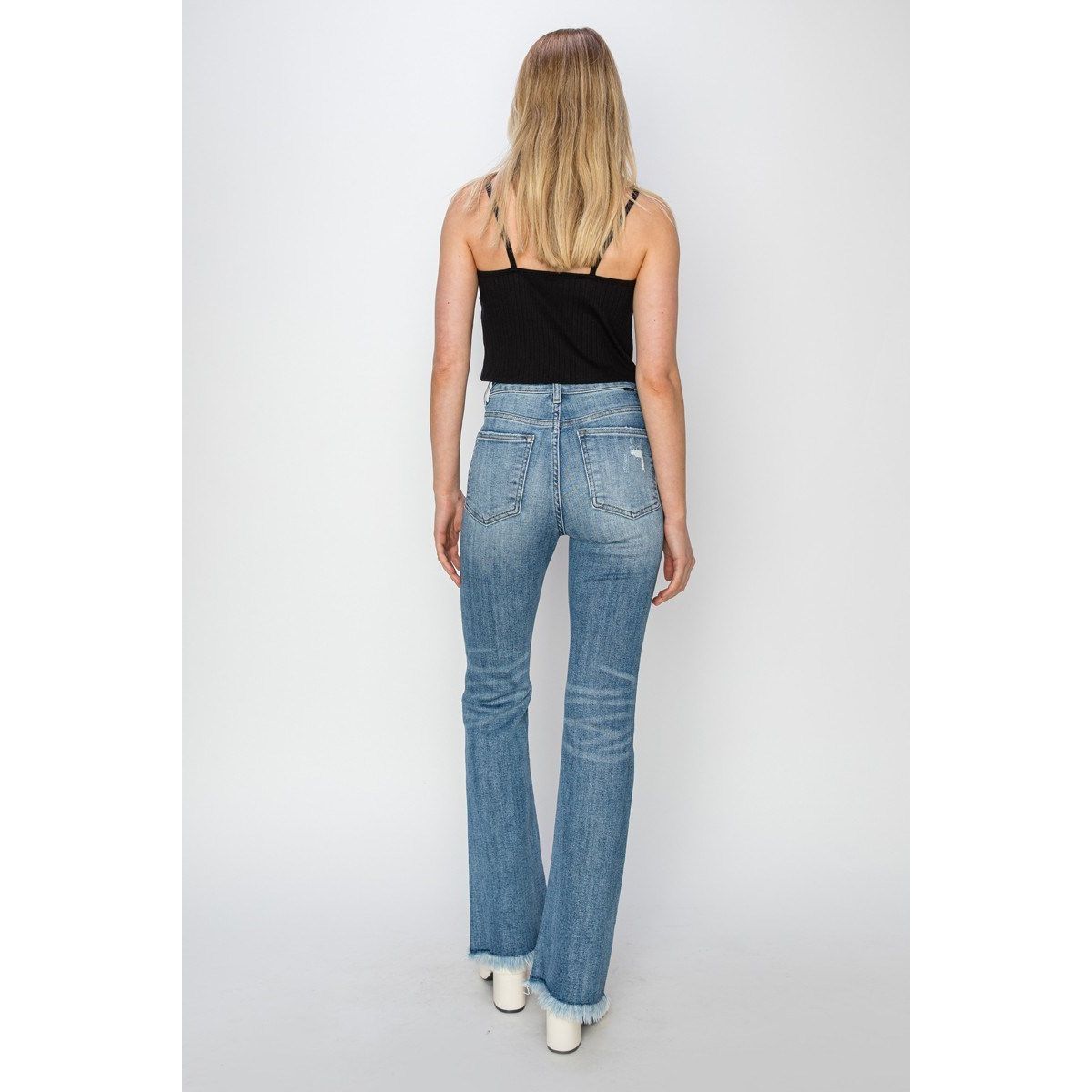 Woman wearing a black top and blue jeans with a frayed hem against a white background