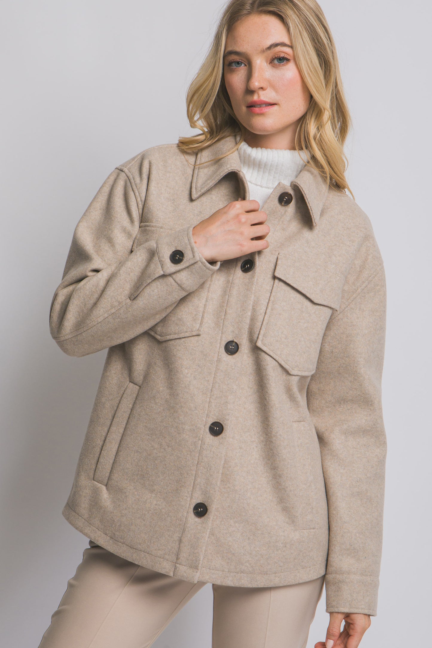 Woman wearing a beige coat with black buttons on a plain background