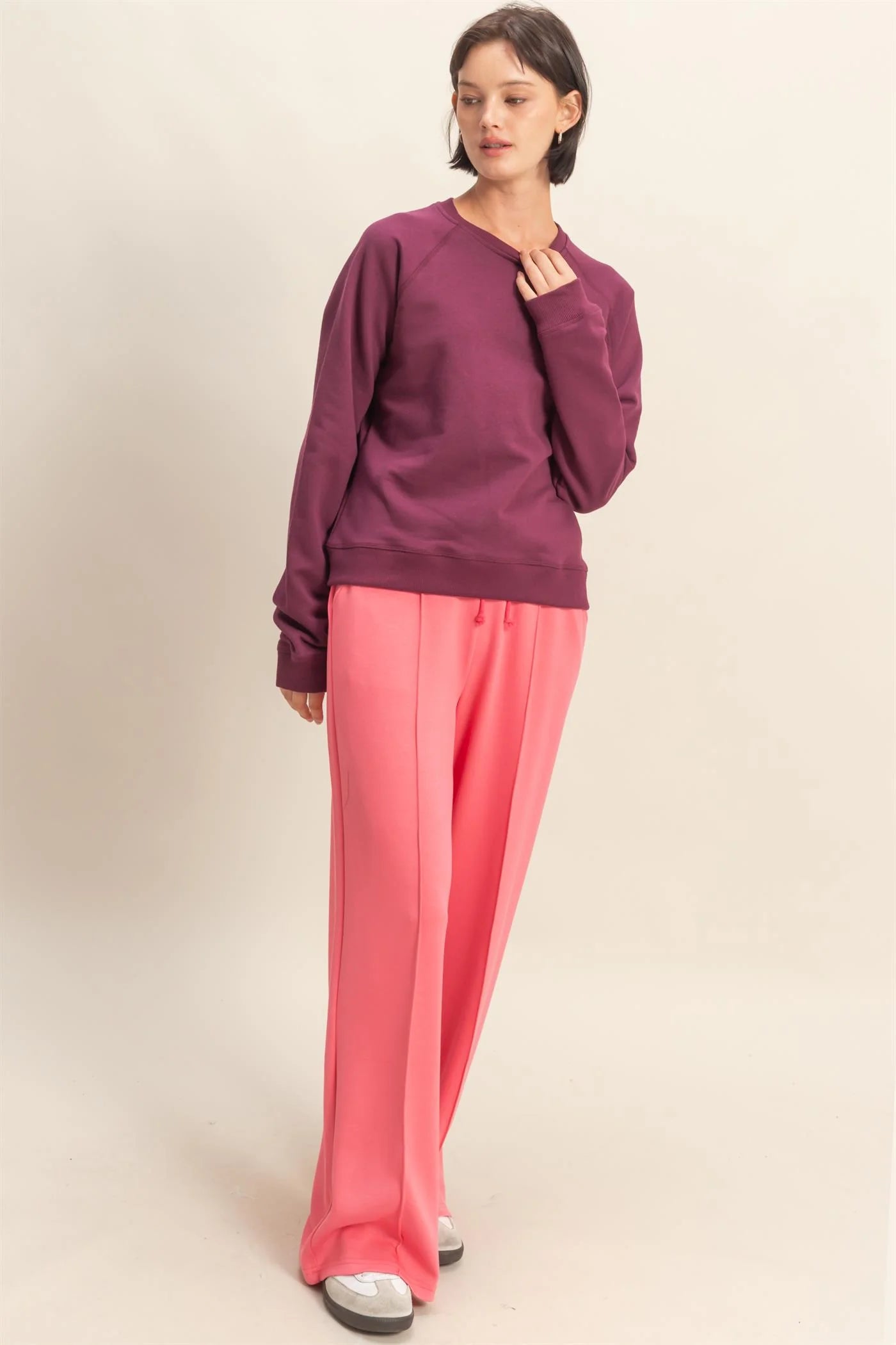 Woman wearing a Dark Cherry sweatshirt and pink pants on a beige background