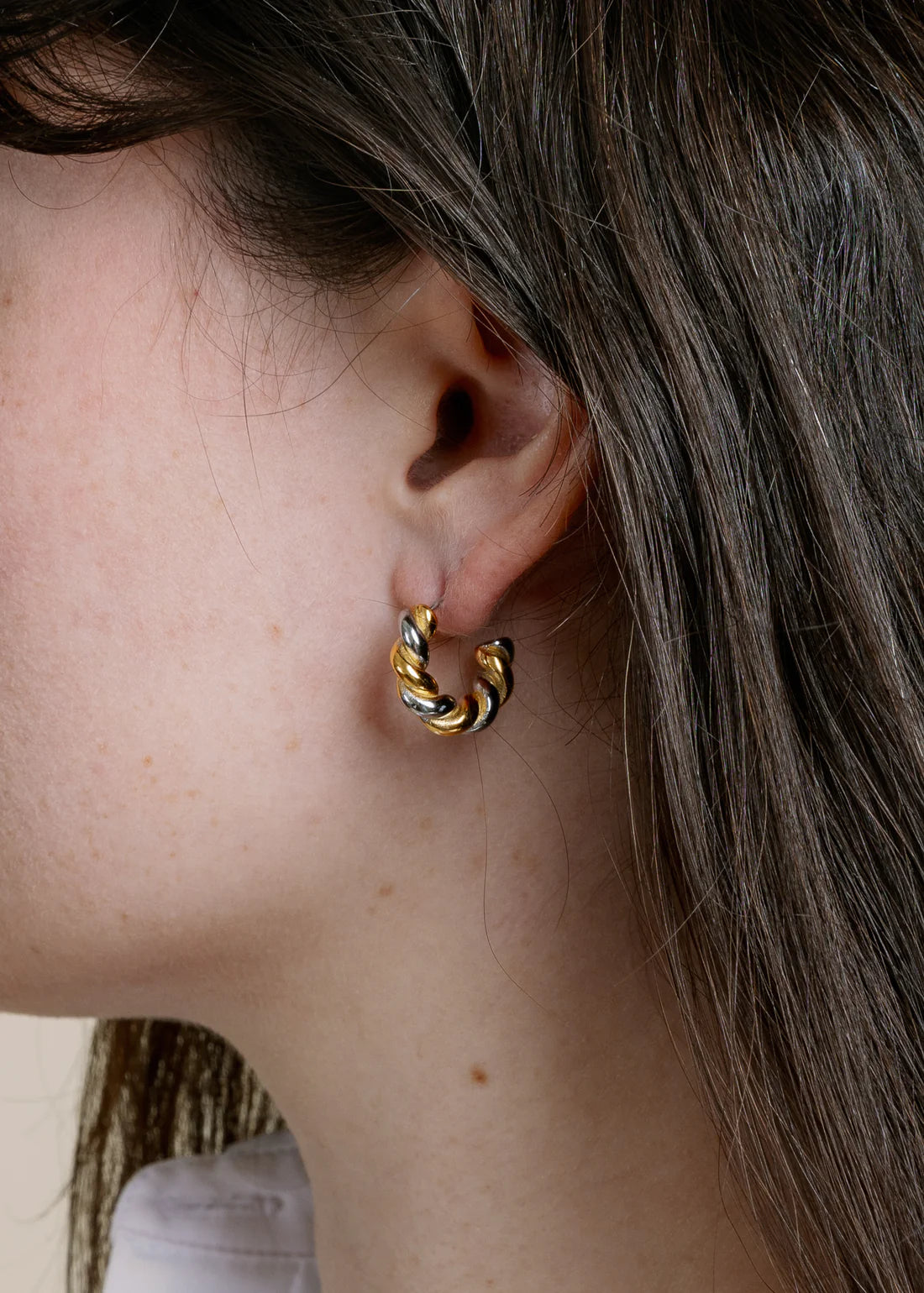 Close-up of a person wearing a gold hoop earring with a blurred background
