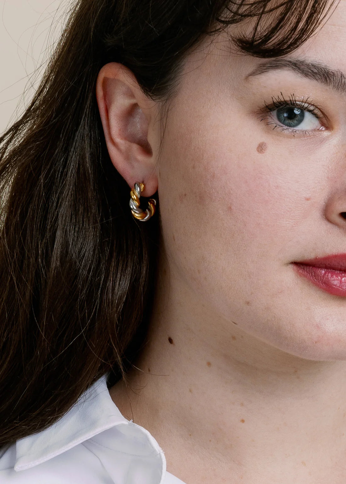 Close-up of a person wearing gold hoop earrings with a neutral background