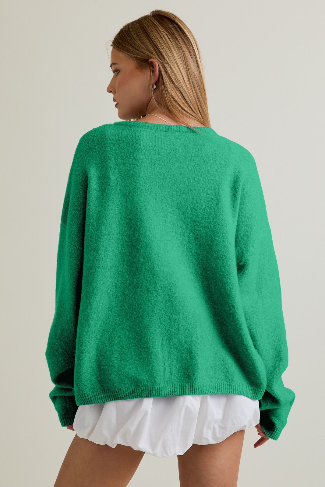 Person wearing a clover green cardigan and white shorts on a plain background
