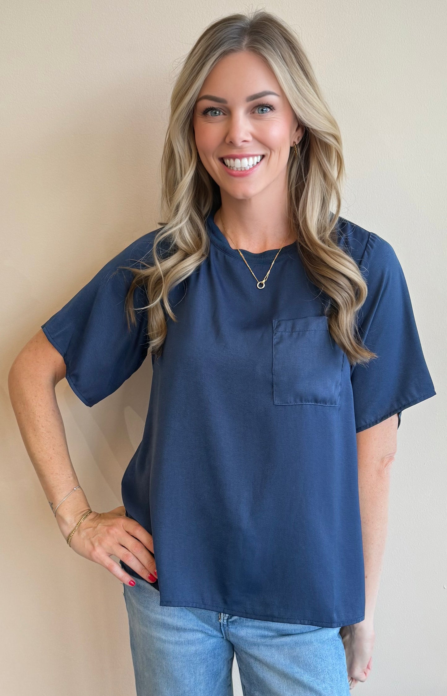 Woman wearing a navy blue top with a pocket against a beige wall