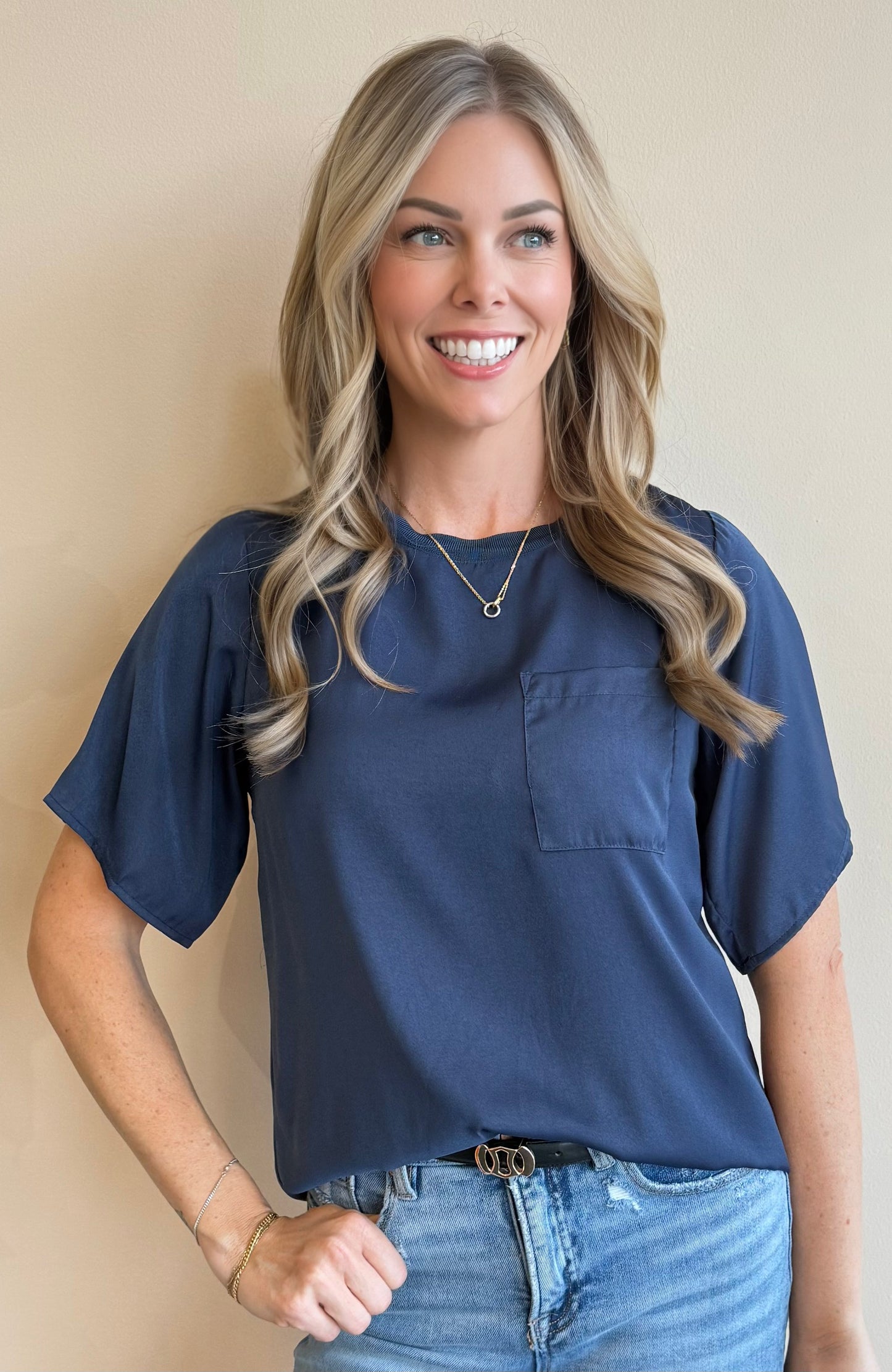 Woman wearing a navy top and jeans against a beige background