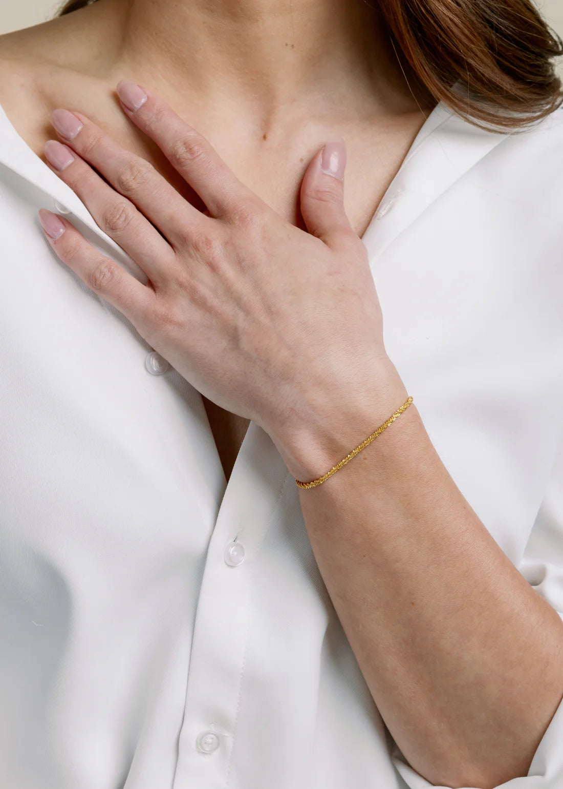 Person wearing a gold bracelet on a white background