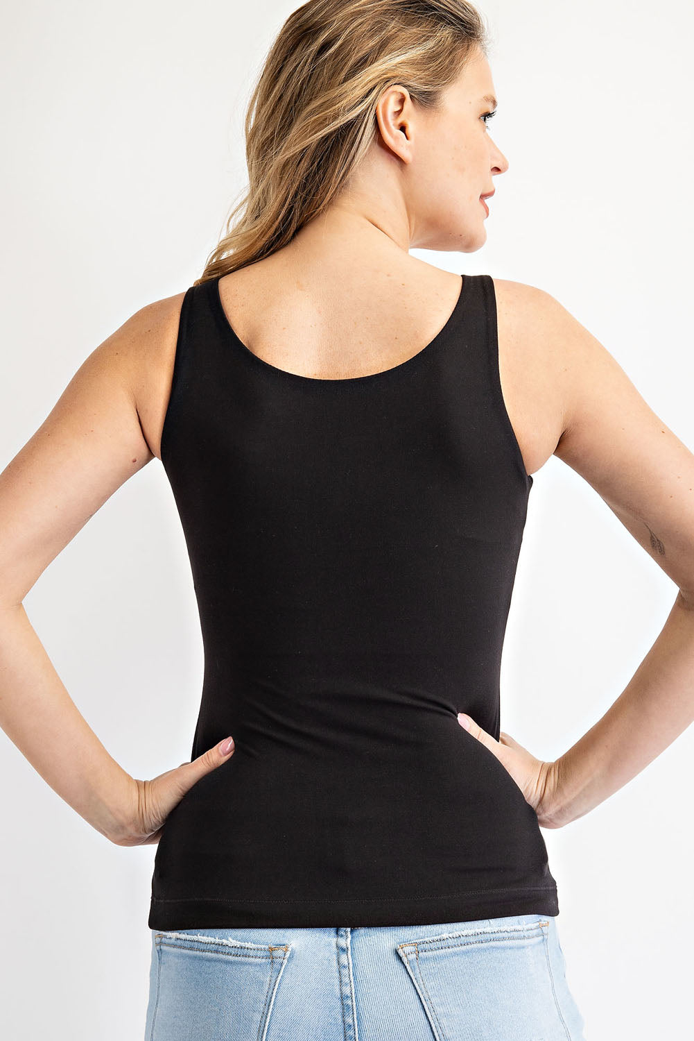 Woman wearing a black tank top and light blue jeans on a white background