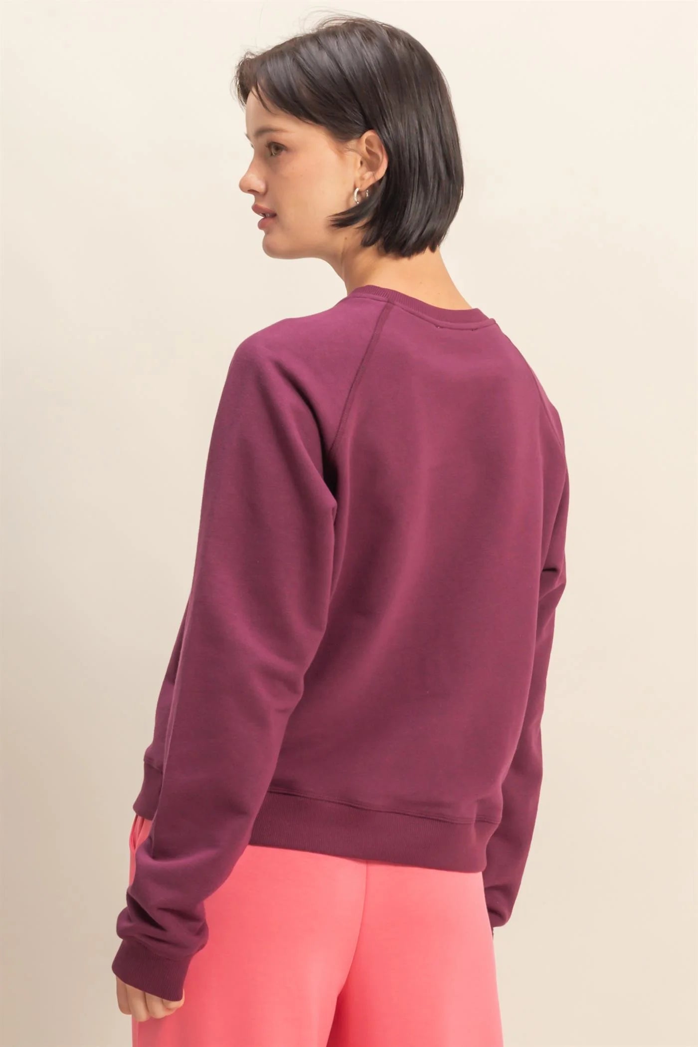 Woman wearing a dark cherry maroon sweatshirt and pink pants on a beige background