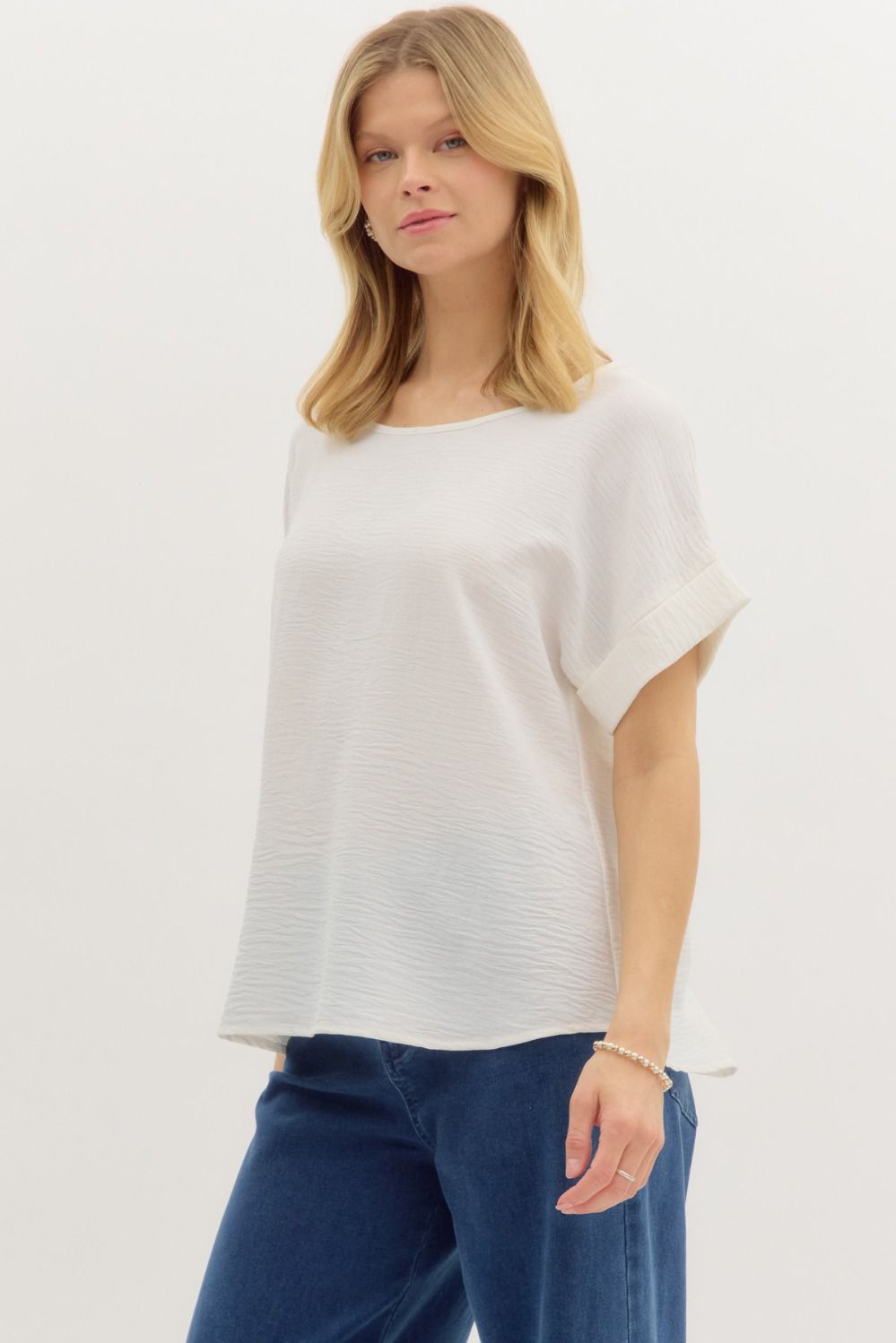 Woman wearing a white short, cuffed sleeve blouse and blue jeans on a plain background
