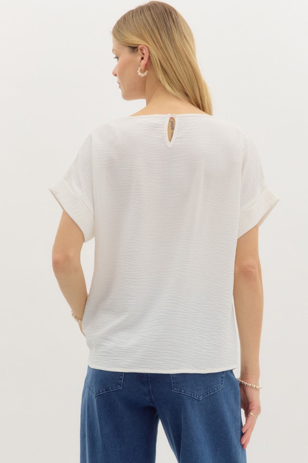 Woman wearing a white t-shirt with a small neck cutout design on the back, standing against a plain background.