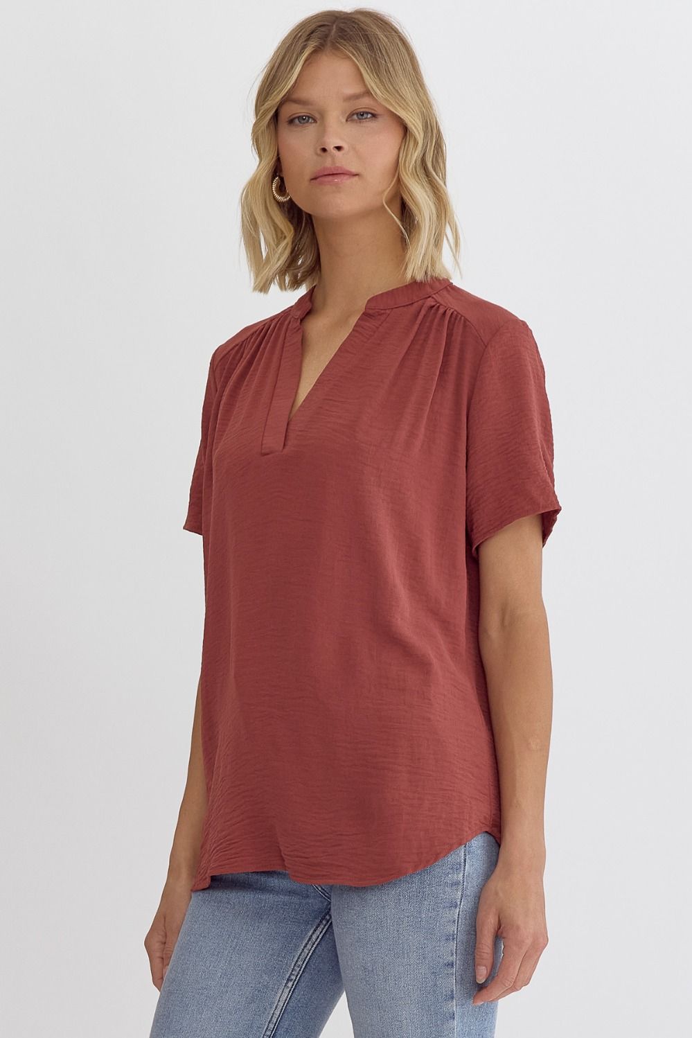 Woman wearing a rust-colored top and blue jeans on a white background