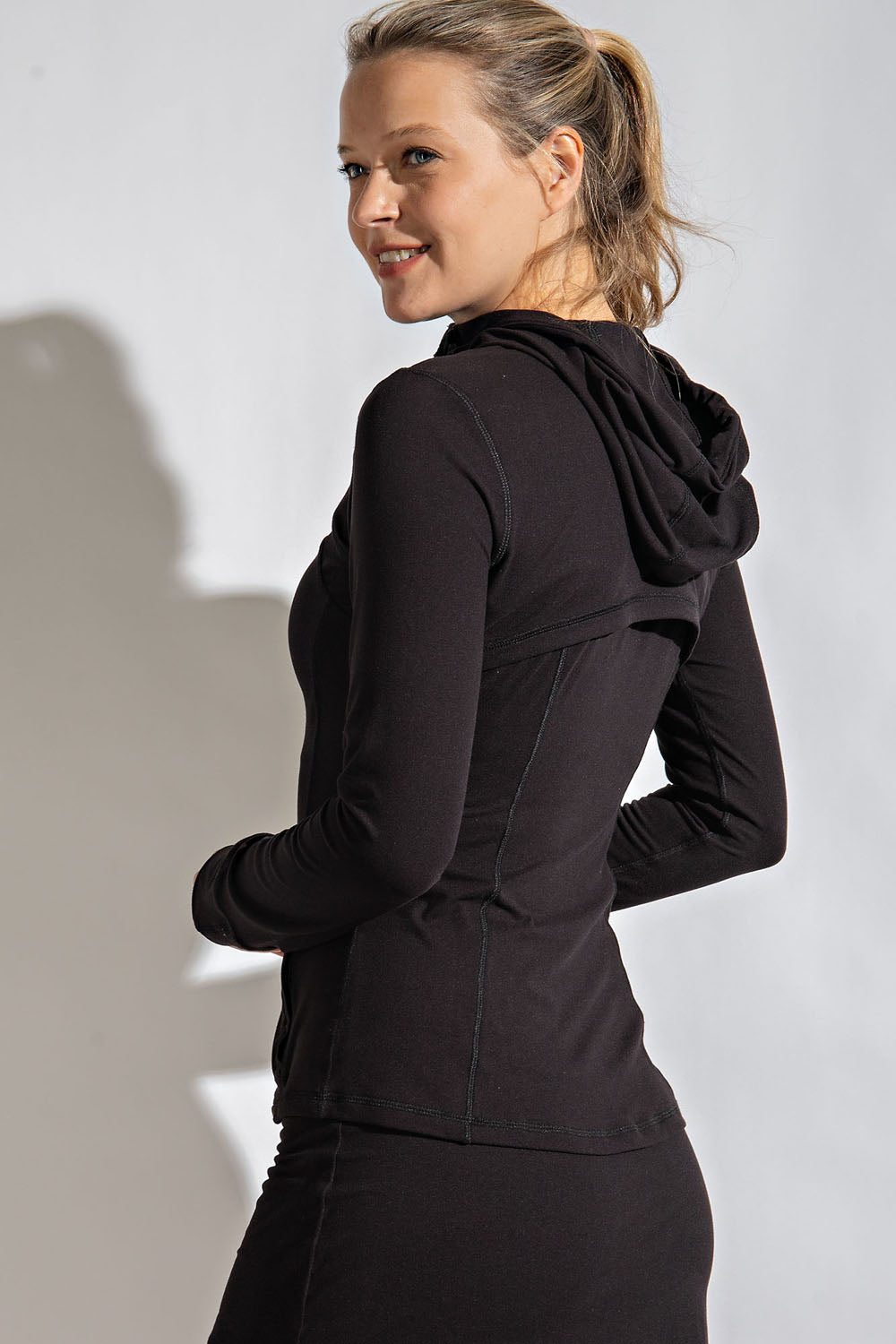 Woman turned toward the back wearing a black hoodie against a plain background