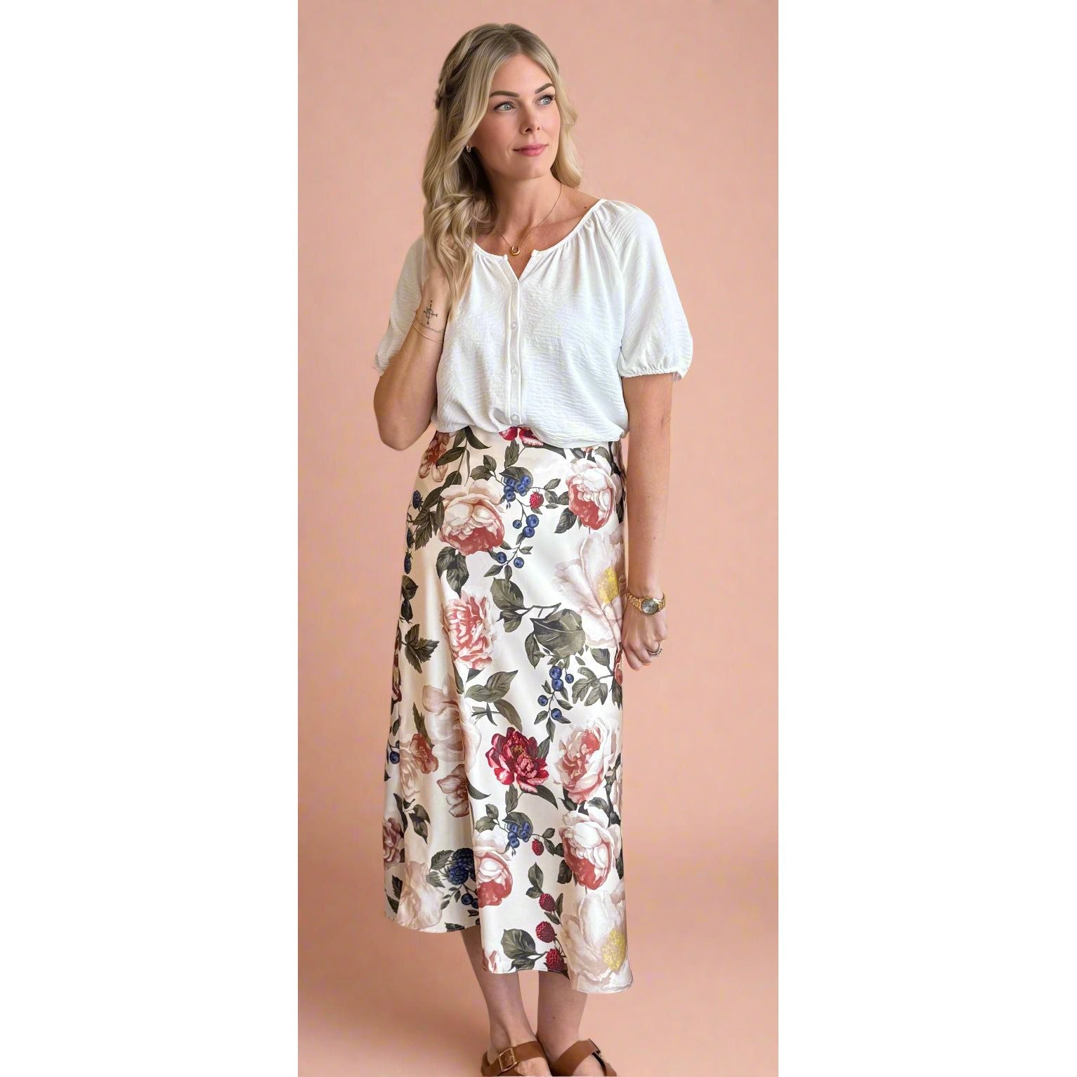 Woman wearing a white blouse and floral skirt against a beige wall.