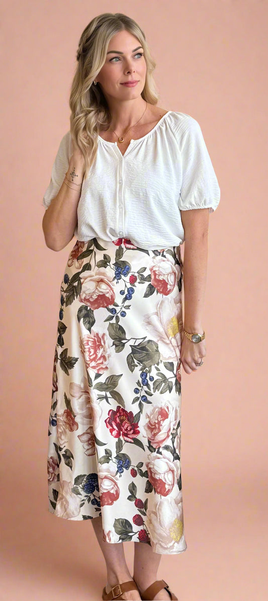 Woman wearing a white blouse and floral skirt against a beige wall.