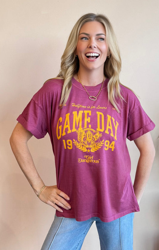 Woman wearing a maroon 'Game Day 1994' t-shirt with yellow text against a beige background
