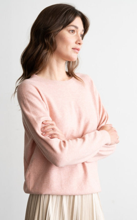 Woman wearing a pink sweater and beige pleated skirt on a white background