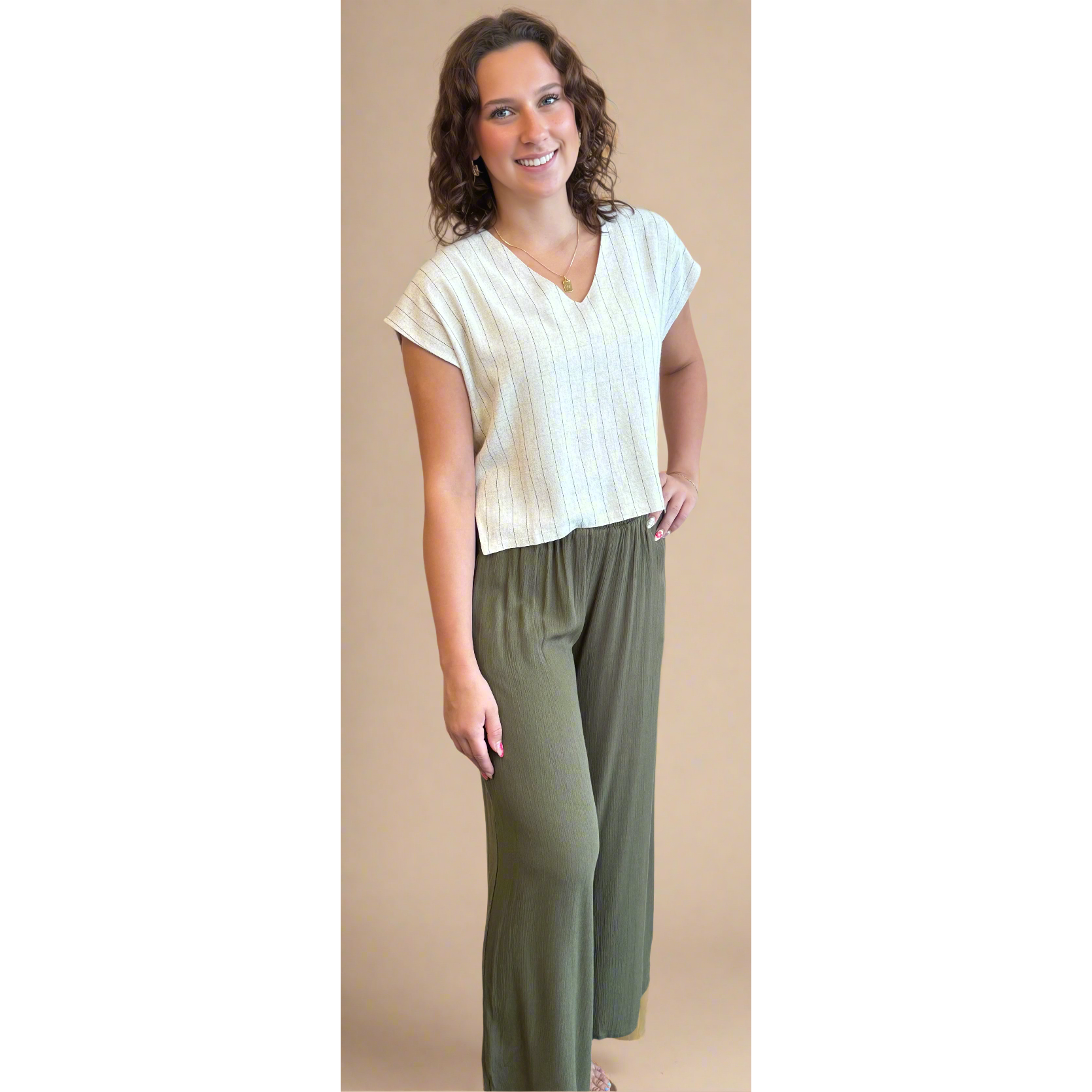 Woman wearing a white top and green pants against a beige wall.