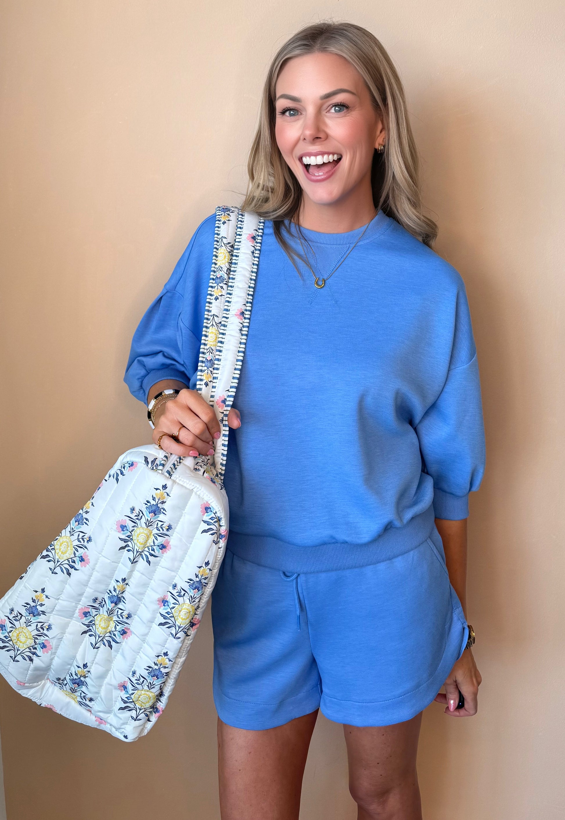 Woman in blue outfit holding a floral bag against a beige background