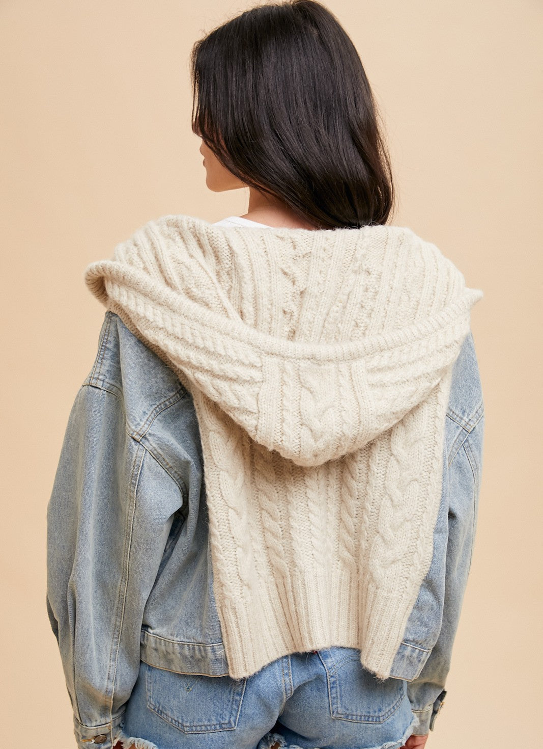 Person wearing a denim jacket over a cream knit sweater on a beige background