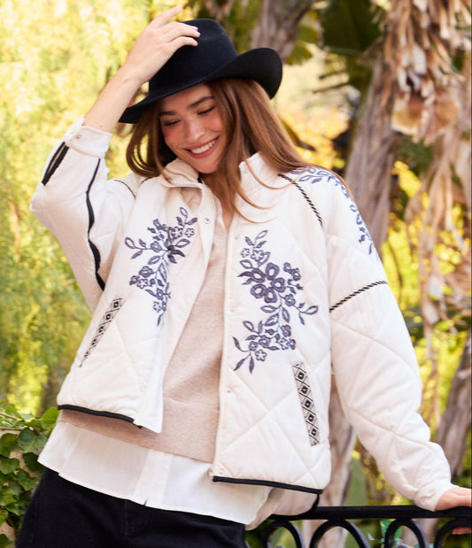 Woman wearing a white jacket with floral embroidery in an outdoor setting